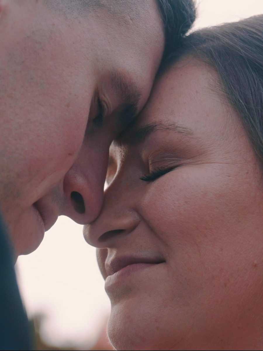 Close-up of a bride and groom with eyes closed and foreheads touching, in soft afternoon light
